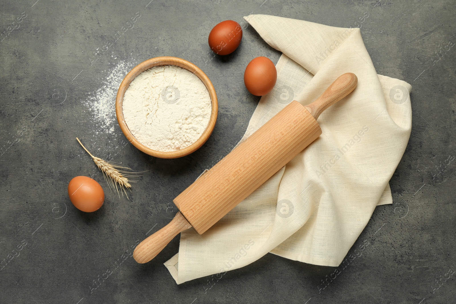 Photo of Rolling pin, bowl of flour, eggs and spike on grey table, flat lay