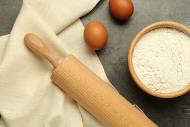 Photo of Rolling pin, bowl of flour and eggs on grey table, flat lay