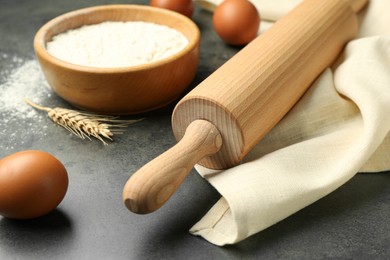 Photo of Rolling pin, bowl of flour, eggs and spike on grey table, closeup