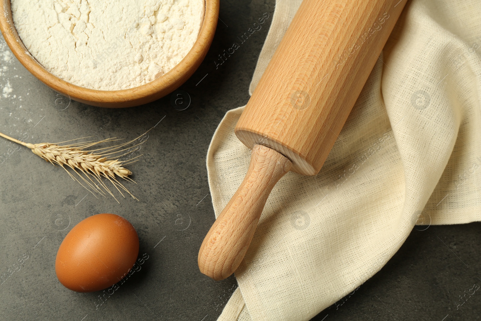 Photo of Rolling pin, bowl of flour, egg and spike on grey table, flat lay