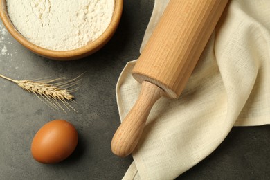 Photo of Rolling pin, bowl of flour, egg and spike on grey table, flat lay