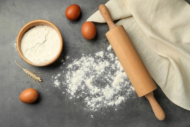 Photo of Rolling pin, bowl of flour, eggs and spike on grey table, flat lay