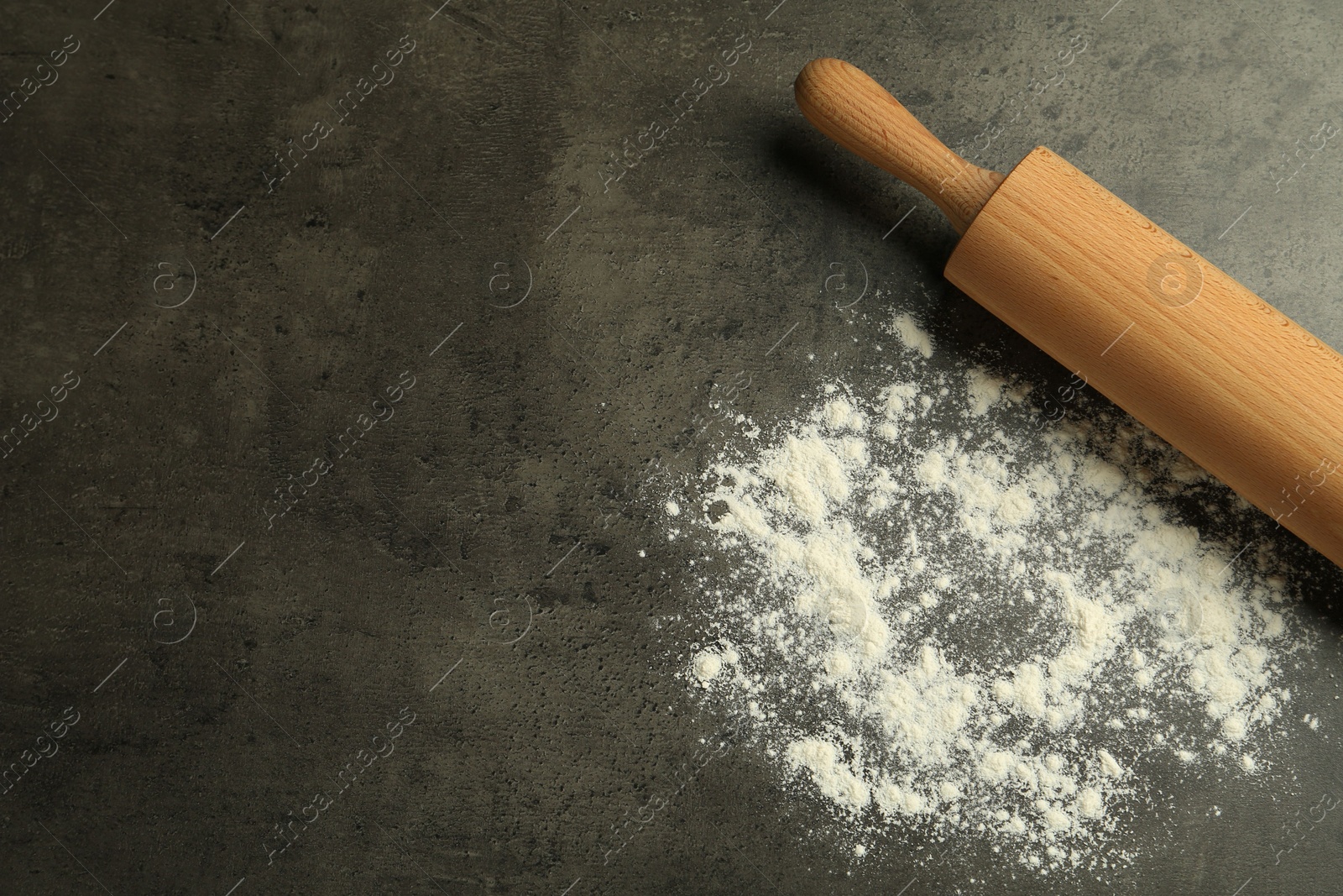 Photo of Wooden rolling pin and flour on grey table, top view. Space for text