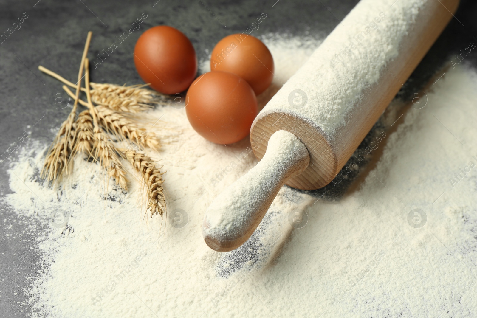 Photo of Wooden rolling pin, eggs, flour and spikes on grey table, closeup