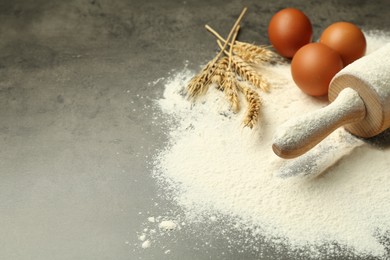 Photo of Wooden rolling pin, eggs, flour and spikes on grey table, closeup. Space for text