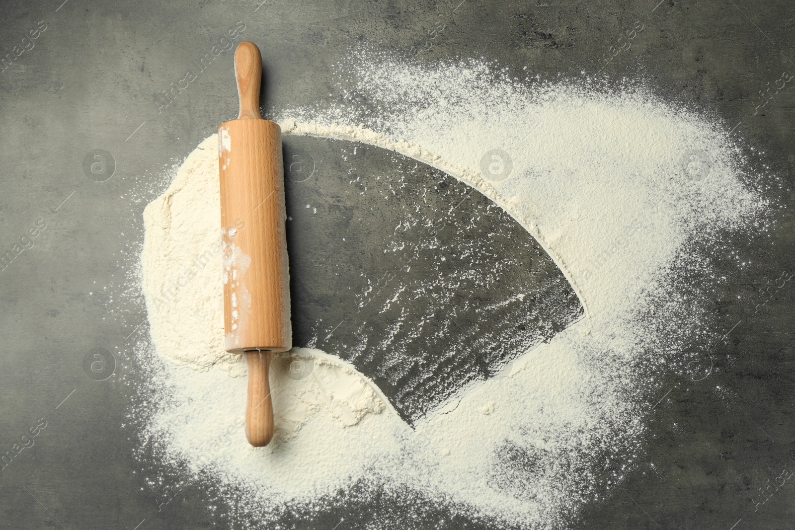 Photo of Wooden rolling pin and flour on grey table, top view. Space for text