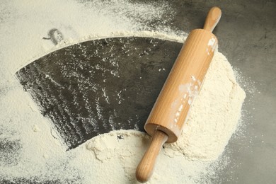 Photo of Wooden rolling pin and flour on grey table, above view. Space for text