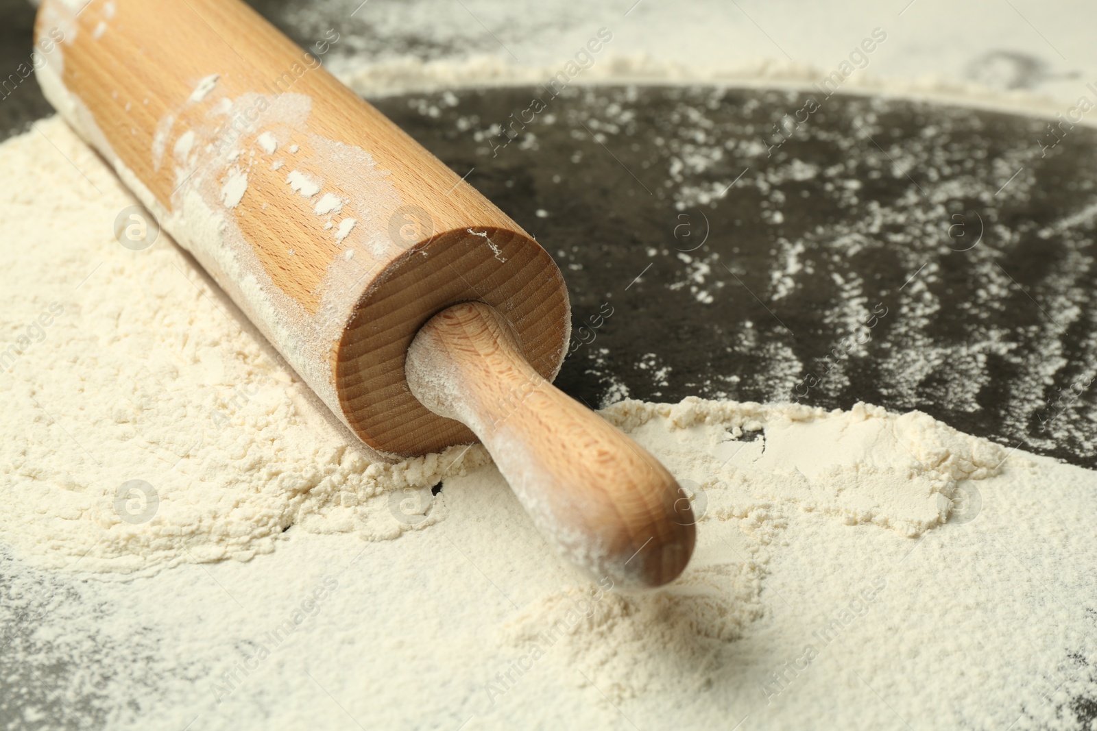 Photo of Wooden rolling pin and flour on grey table, closeup. Space for text