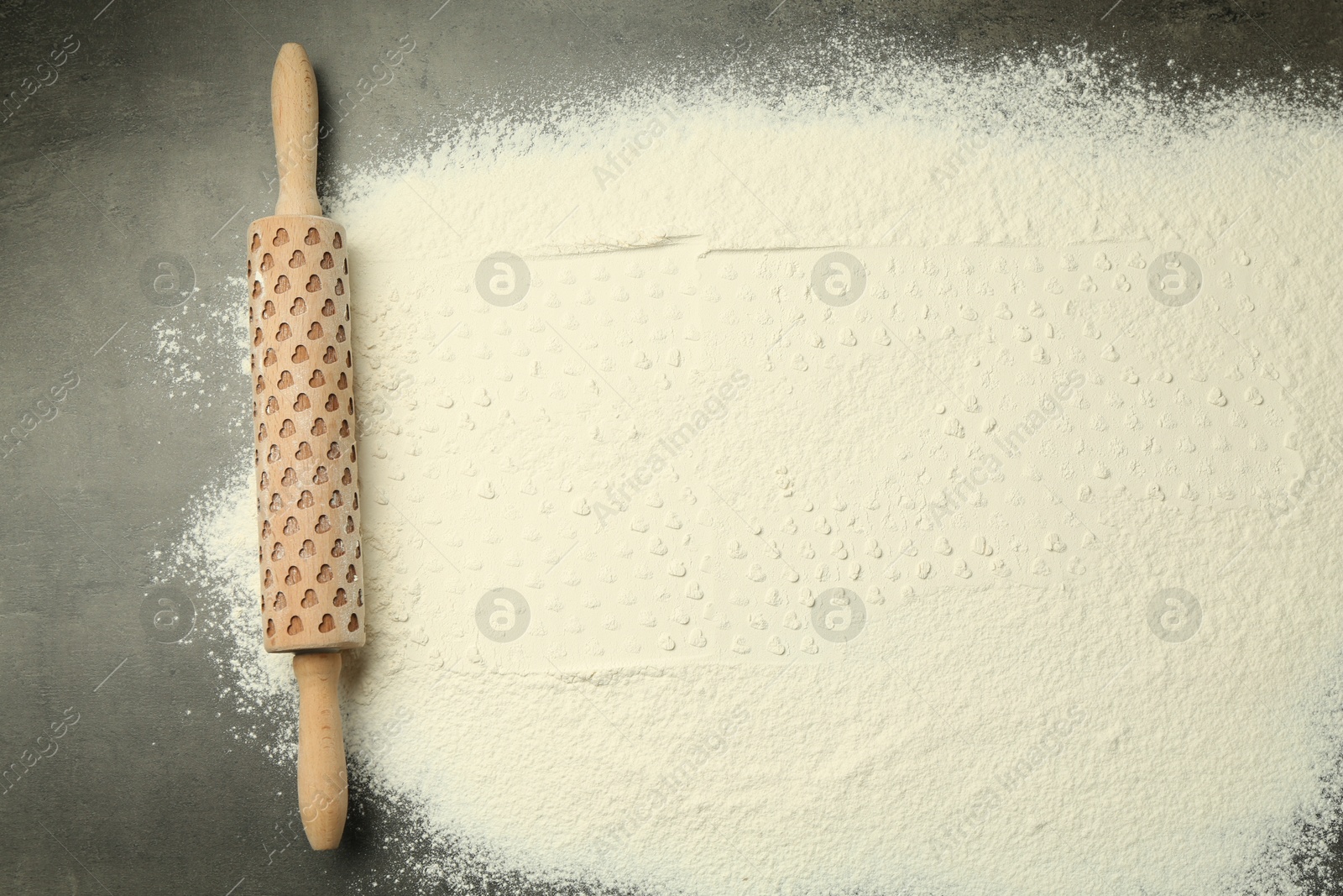 Photo of Wooden rolling pin and flour on grey table, top view. Space for text