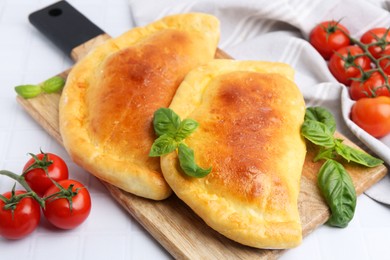 Photo of Tasty vegetarian calzones with basil and tomatoes on white tiled table, closeup