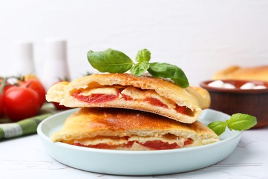 Photo of Pieces of tasty vegetarian calzone with tomato, cheese and basil on white textured table, closeup