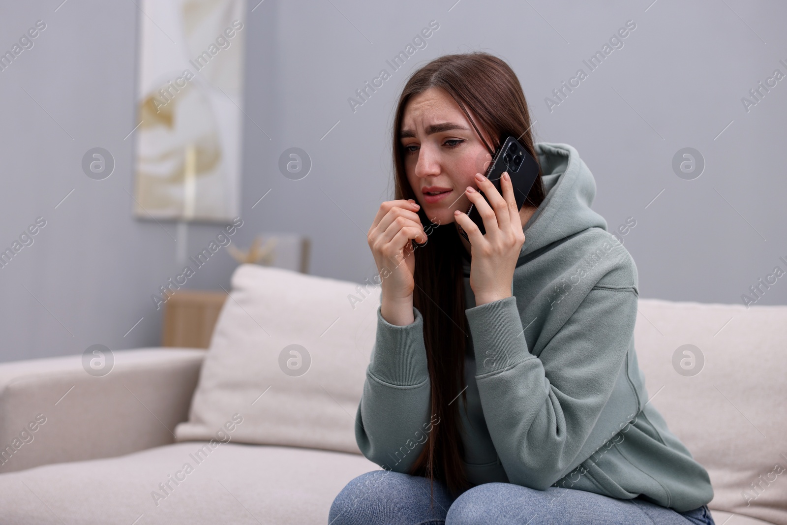 Photo of Depressed woman calling hotline for mental health help on sofa at home