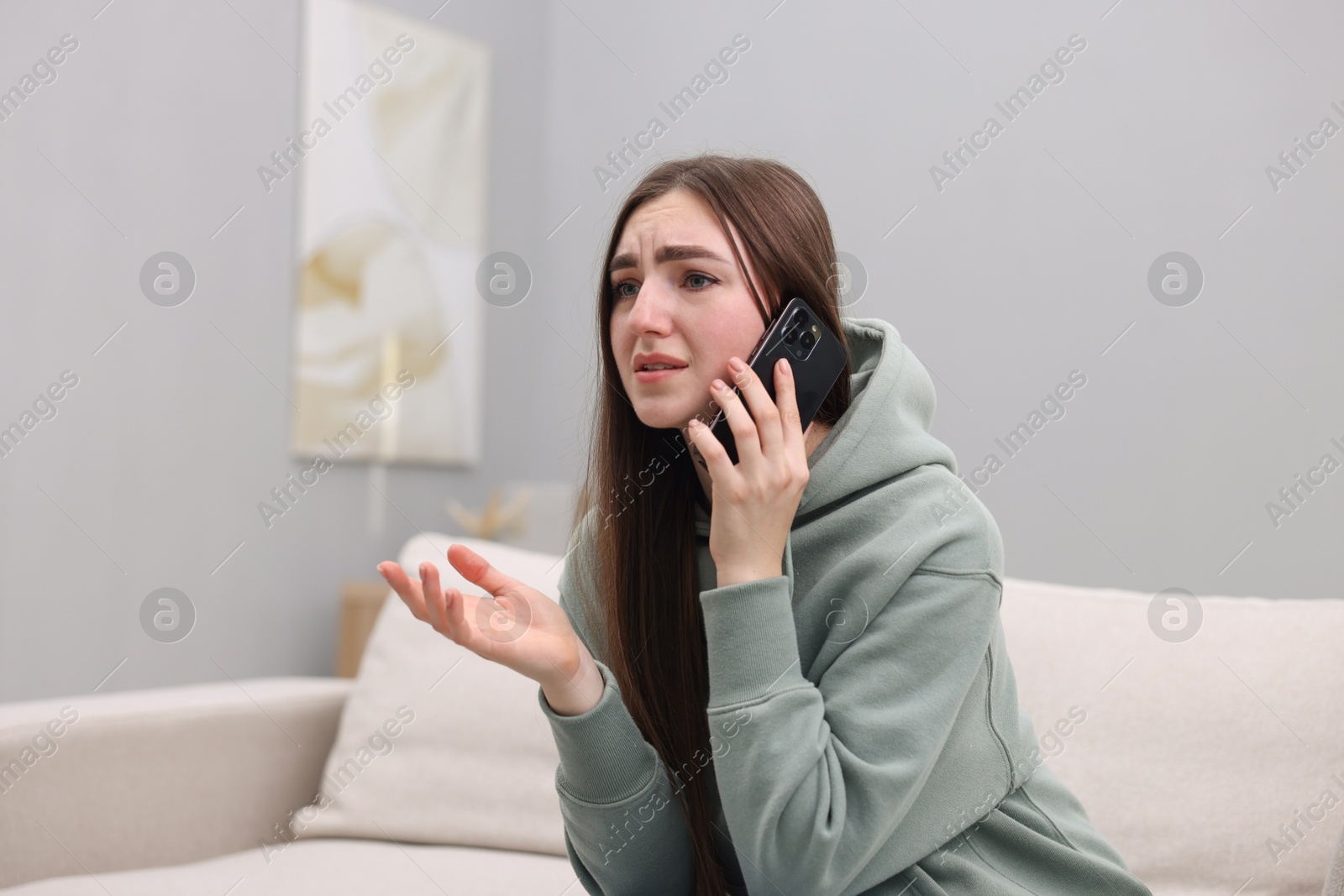 Photo of Depressed woman calling hotline for mental health help on sofa at home