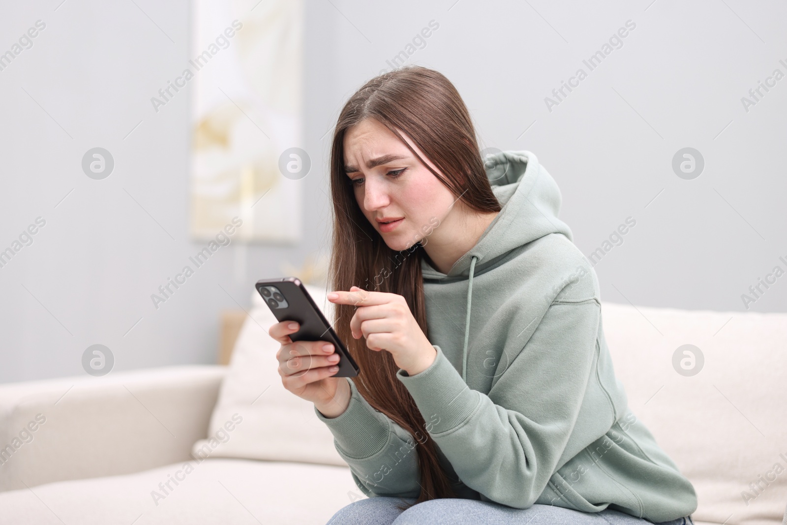 Photo of Depressed woman calling hotline for mental health help on sofa at home