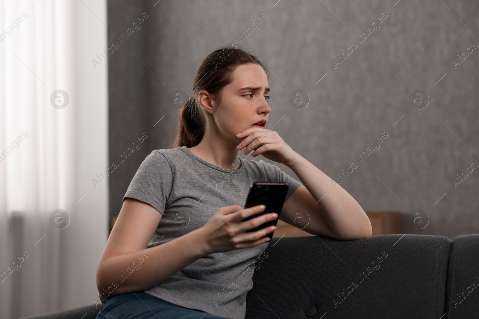 Photo of Depressed woman calling hotline for mental health help on sofa at home