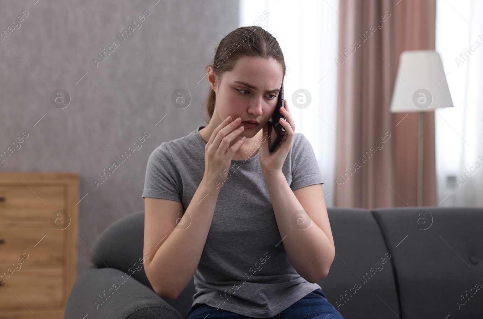 Photo of Depressed woman calling hotline for mental health help on sofa at home