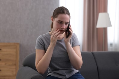 Photo of Depressed woman calling hotline for mental health help on sofa at home