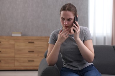 Photo of Depressed woman calling hotline for mental health help on sofa at home. Space for text