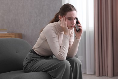 Photo of Depressed woman calling hotline for mental health help on sofa at home