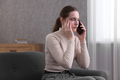 Photo of Depressed woman calling hotline for mental health help on sofa at home