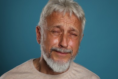 Photo of Sad senior man crying on blue background, closeup