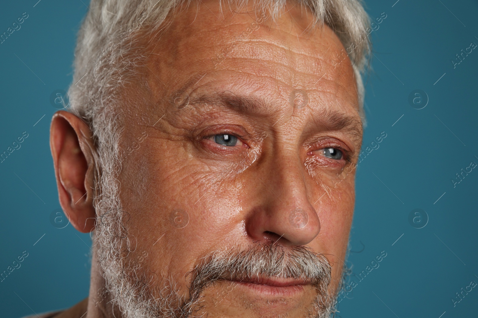 Photo of Sad senior man crying on blue background, closeup