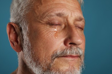 Photo of Sad senior man crying on blue background, closeup