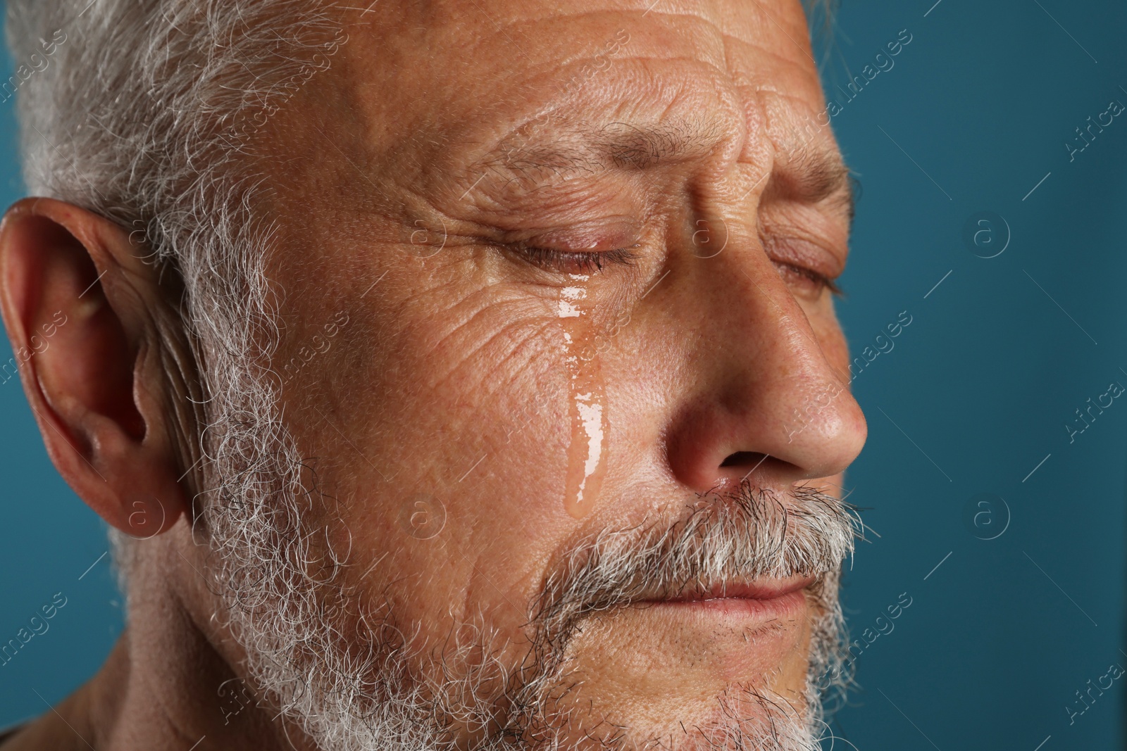 Photo of Sad senior man crying on blue background, closeup