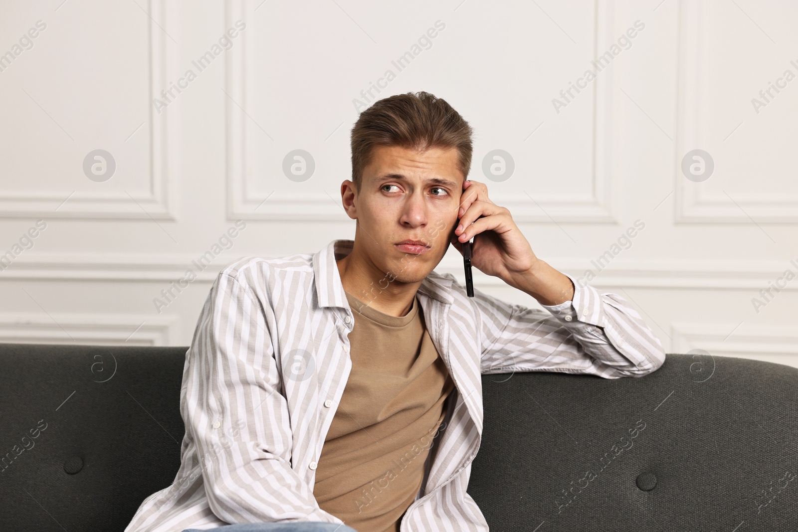 Photo of Stressed man calling hotline for mental health help on sofa at home