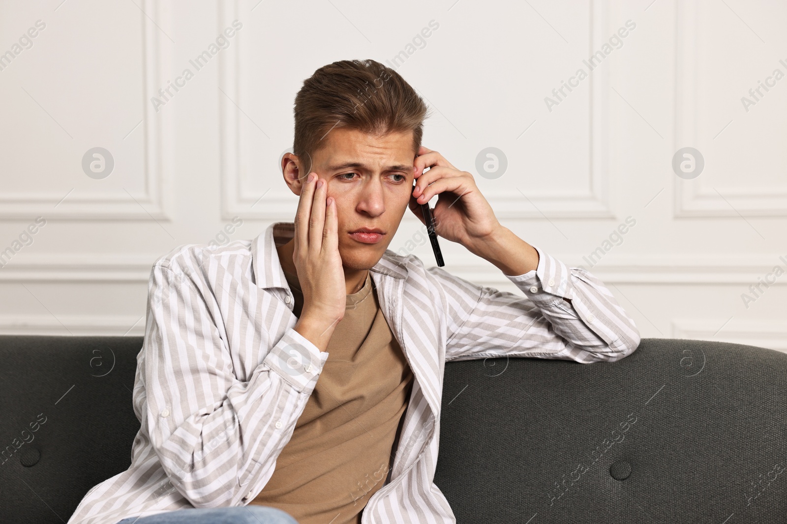 Photo of Worried man calling hotline for mental health help on sofa at home