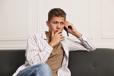 Photo of Worried man calling hotline for mental health help on sofa at home