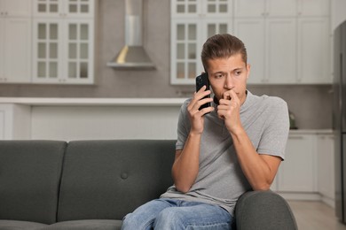 Photo of Stressed man calling hotline for mental health help on sofa in kitchen