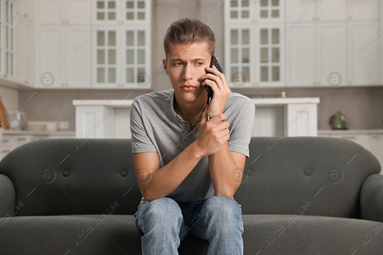 Photo of Stressed man calling hotline for mental health help on sofa in kitchen