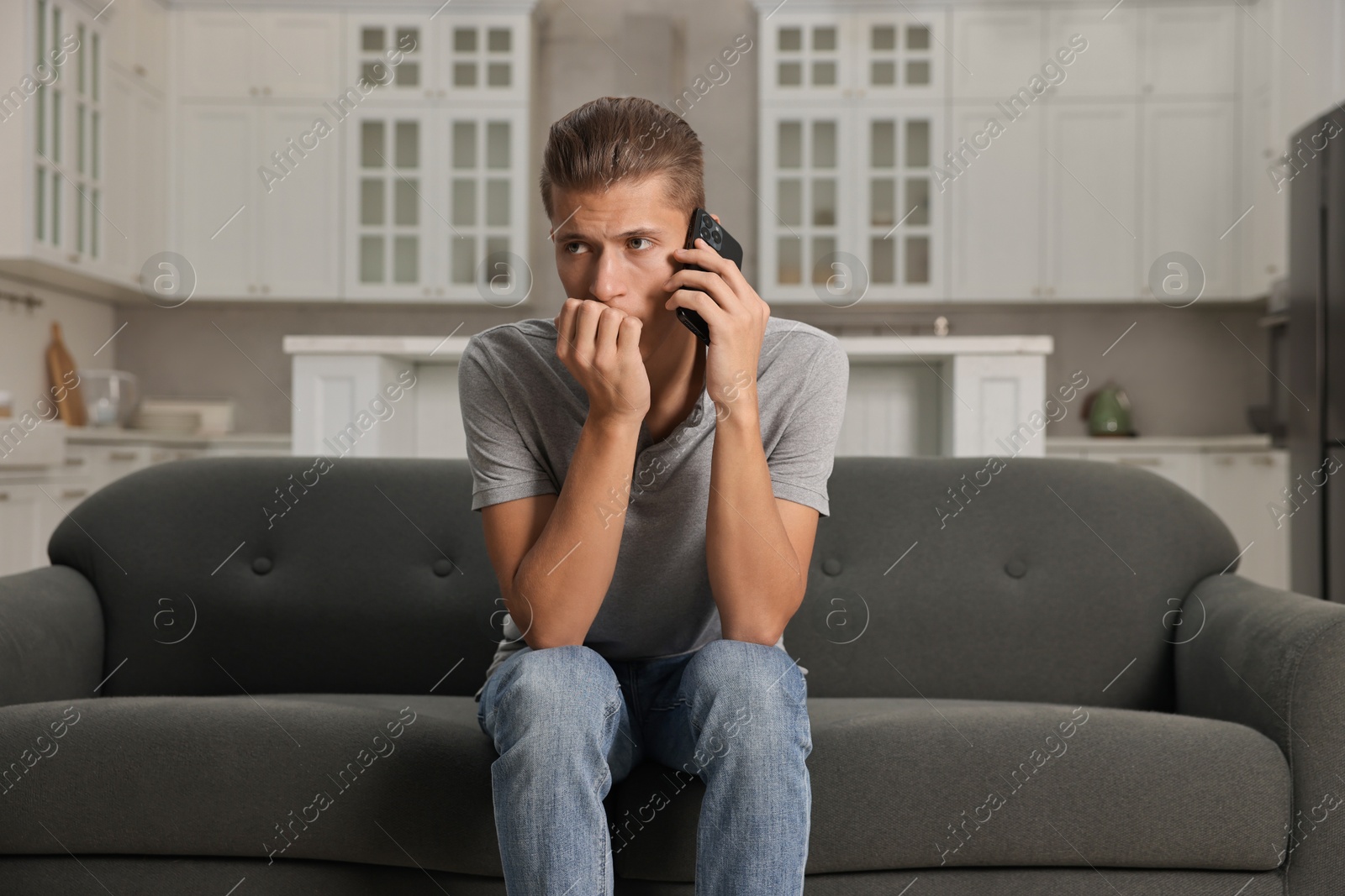 Photo of Stressed man calling hotline for mental health help on sofa in kitchen