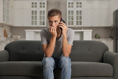 Photo of Stressed man calling hotline for mental health help on sofa in kitchen