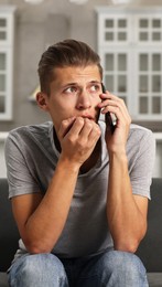 Photo of Stressed man calling hotline for mental health help on sofa in kitchen