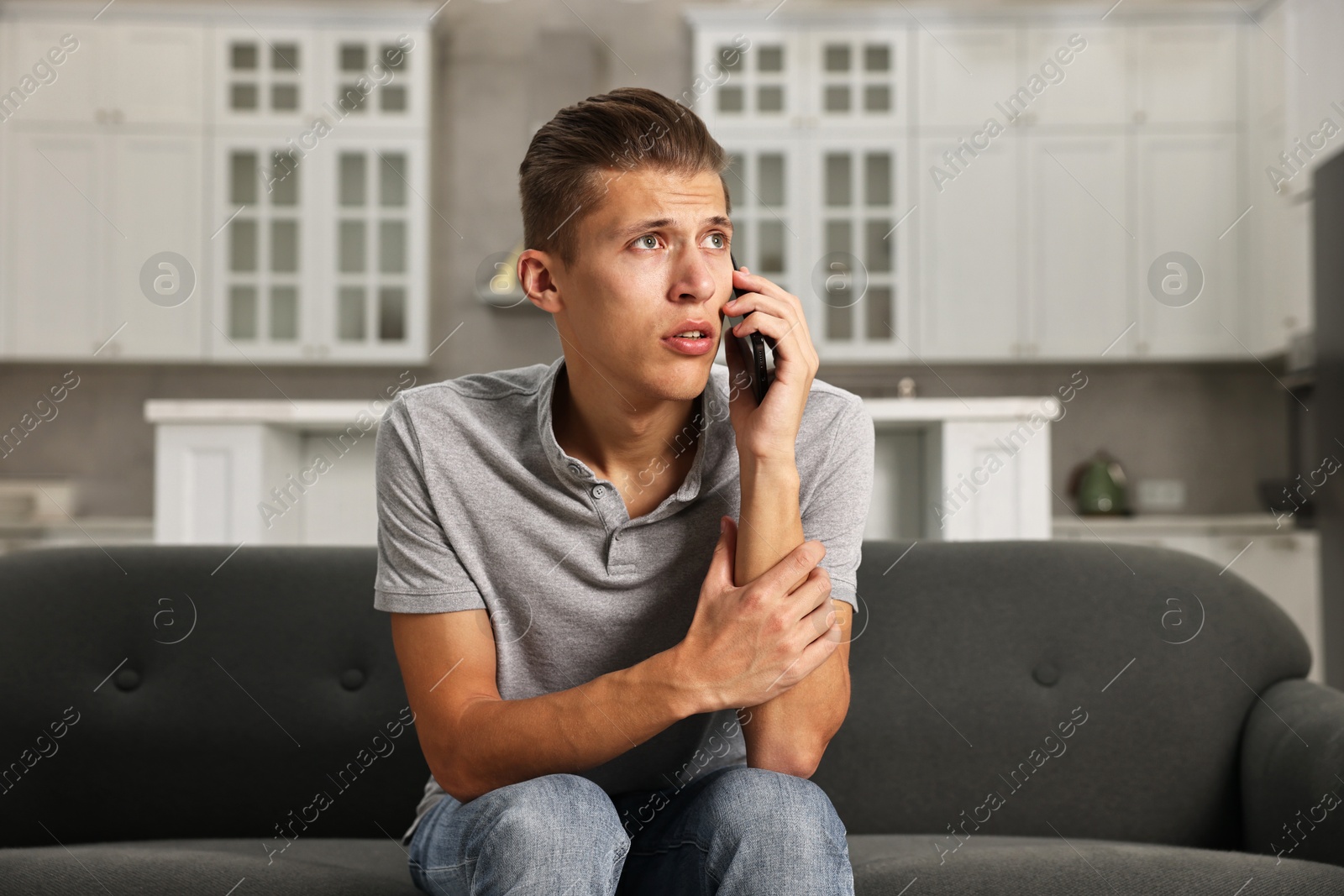 Photo of Stressed man calling hotline for mental health help on sofa in kitchen