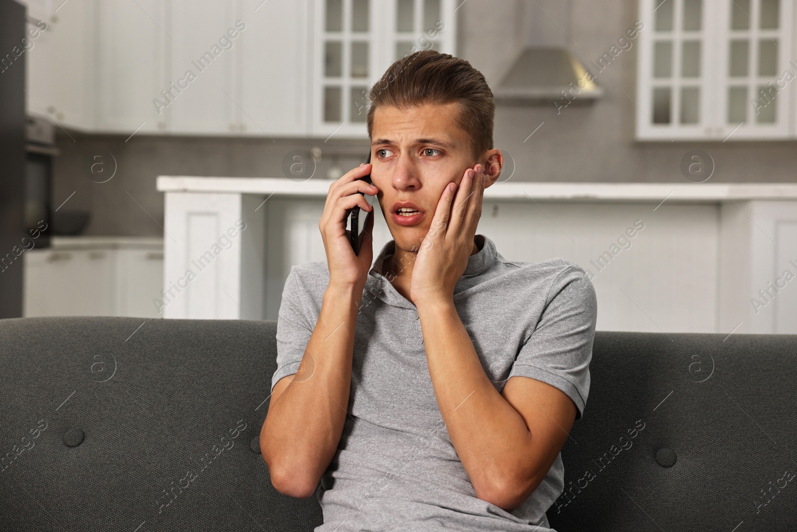 Photo of Stressed man calling hotline for mental health help on sofa in kitchen