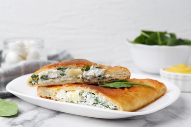 Photo of Pieces of tasty calzone with cheese and basil on white marble table, closeup