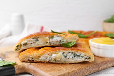 Photo of Pieces of tasty calzone with basil, cheese and sauce on table, closeup