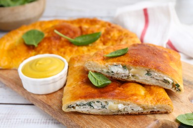 Photo of Tasty calzones with basil, cheese and sauce on white wooden table, closeup