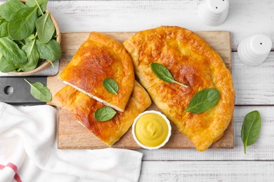 Photo of Tasty calzones with basil, cheese and sauce on white wooden table, flat lay