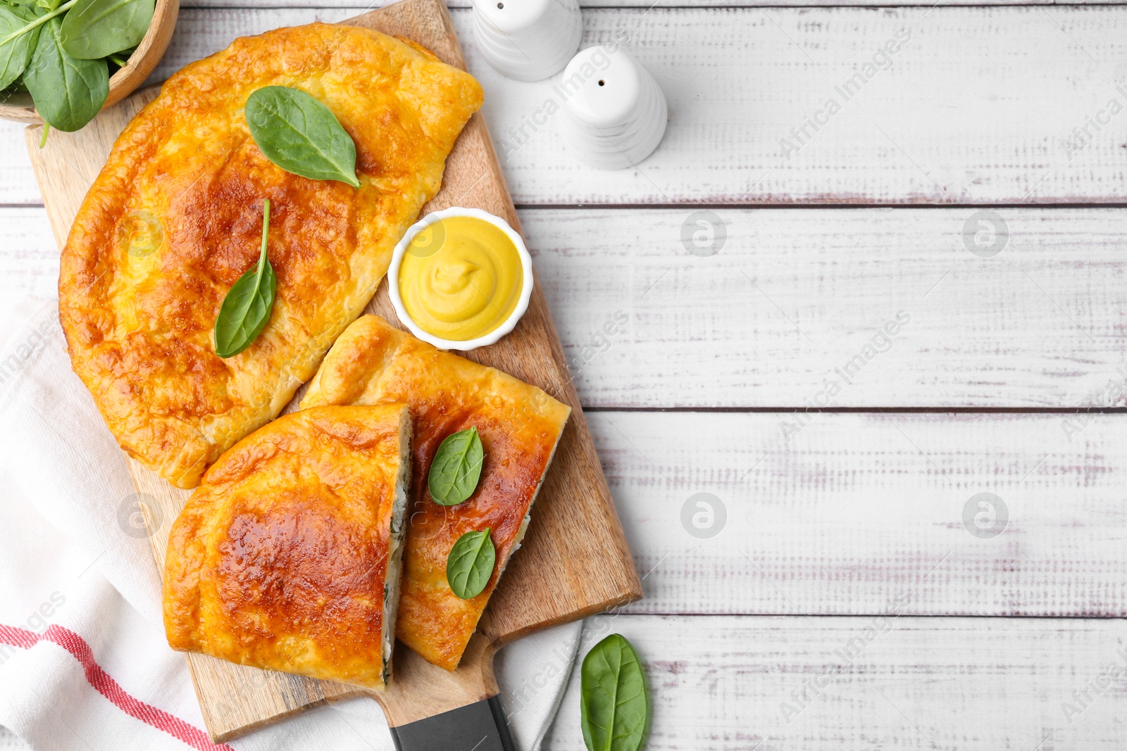 Photo of Tasty calzones with basil, cheese and sauce on white wooden table, flat lay. Space for text