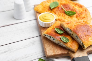 Photo of Tasty calzones with basil, cheese and sauce on white wooden table, closeup. Space for text