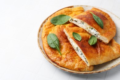 Photo of Tasty calzones with basil and cheese on white tiled table, closeup. Space for text