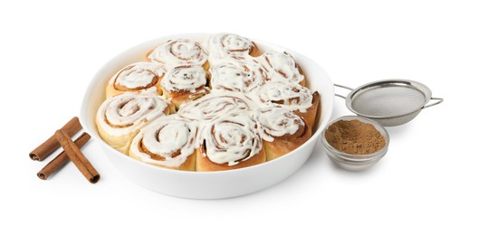 Photo of Delicious frosted cinnamon rolls in baking dish, spices and sieve isolated on white