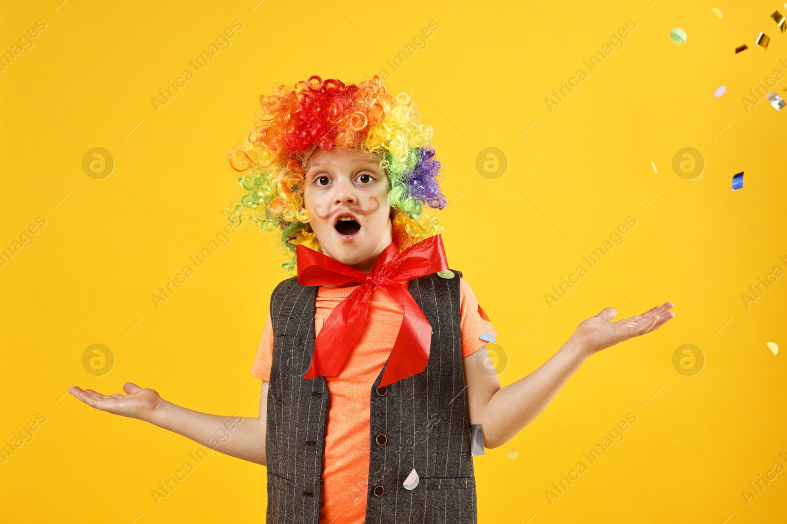 Photo of Surprised boy dressed like clown and flying confetti on orange background. Surprise party