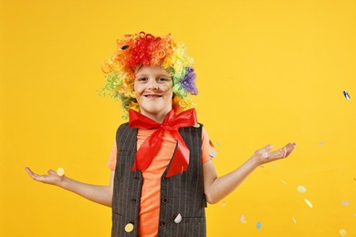 Photo of Happy little boy dressed like clown and flying confetti on orange background. Surprise party