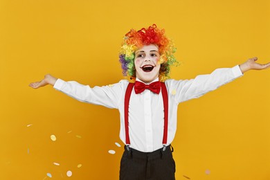 Photo of Happy little boy dressed like clown and flying confetti on yellow background. Surprise party