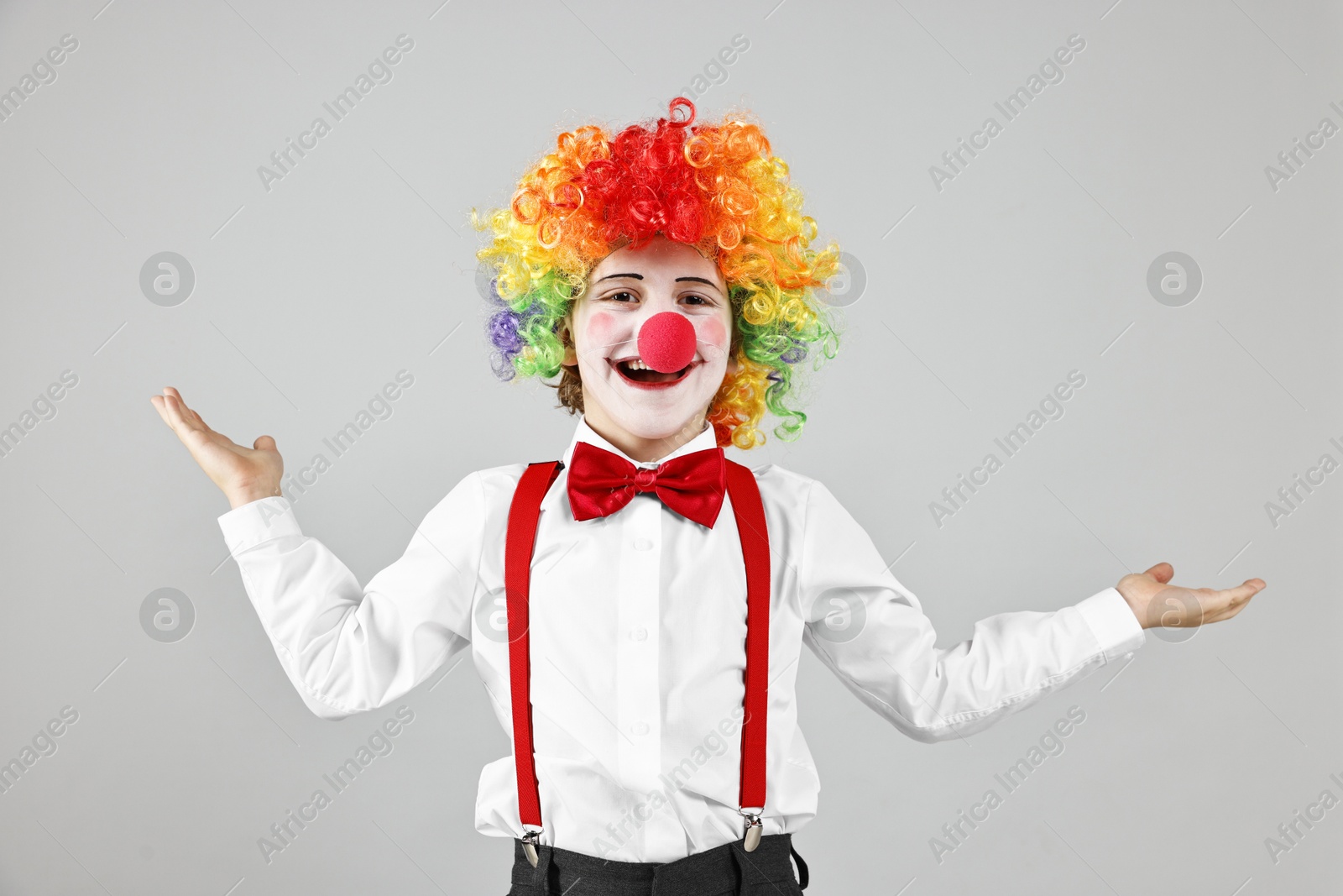 Photo of Happy little boy in clown wig and red nose on grey background. Surprise party